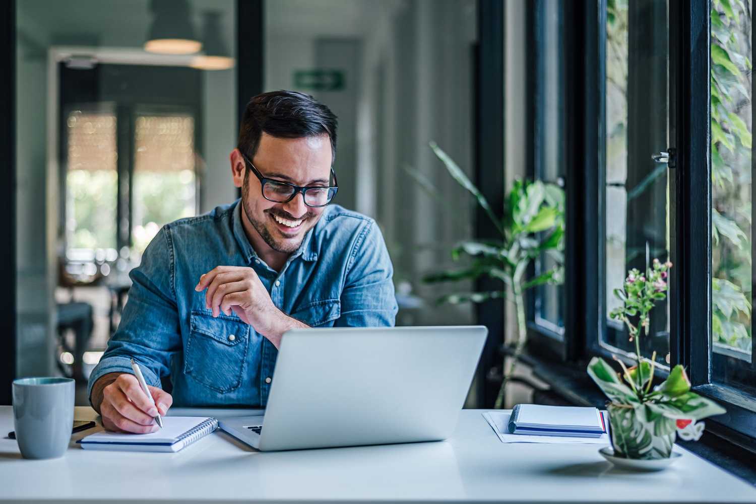 A man smiling at a computer while taking notes