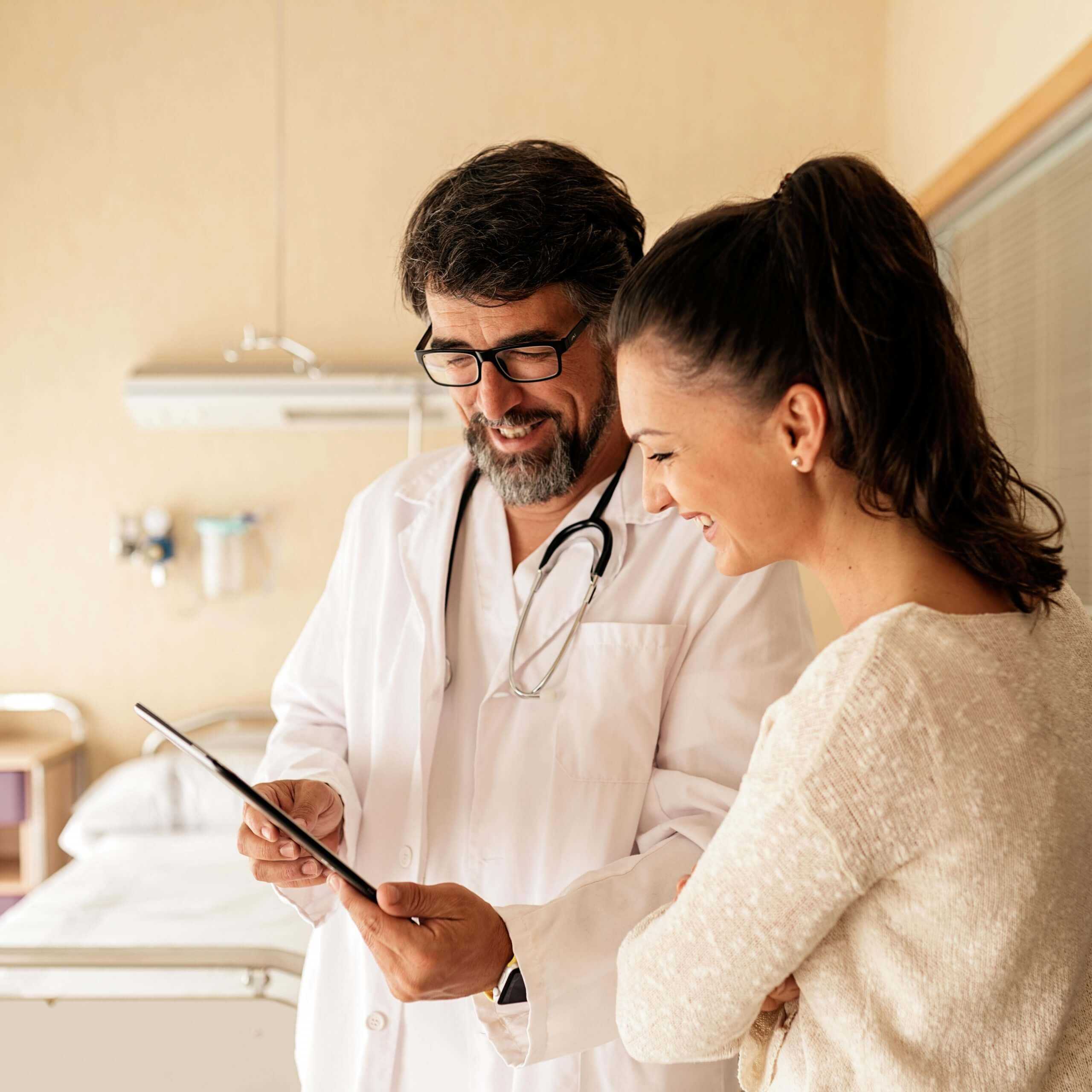 a happy male doctor in corvel's preferred provider network reviewing data on a tablet with a happy female patient