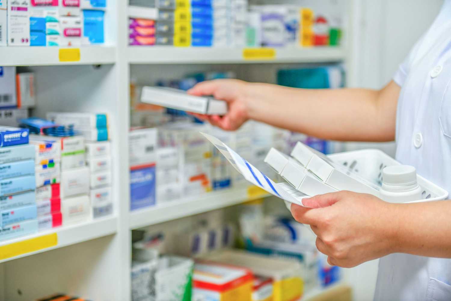 The arms of a pharmacist grabbing medications off of a pharmacy shelf stocked with prescription drugs including generic Nucynta (Tapentadol)