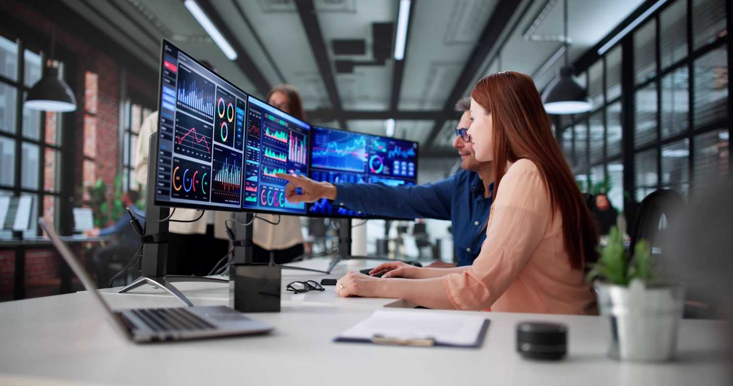 professional woman sitting at a desk with a male colleague pointing at the computer screen to break down data silos in workers comp