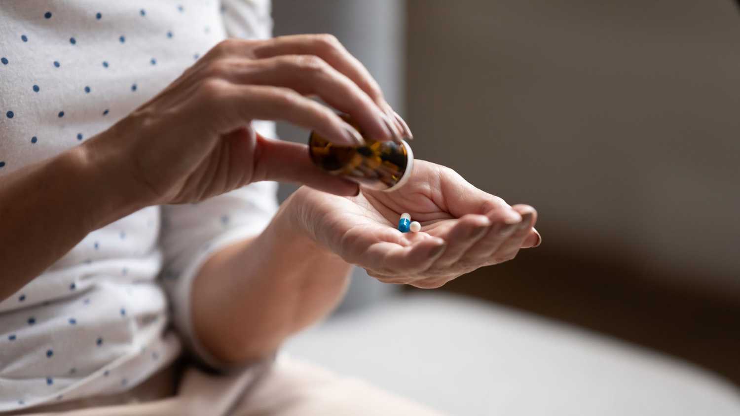 A person holding a medication bottle, and pouring two pills into their hand