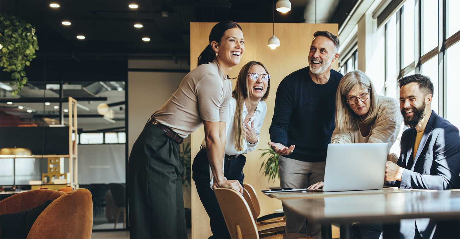 Colleagues standing around a computer smiling and laughing