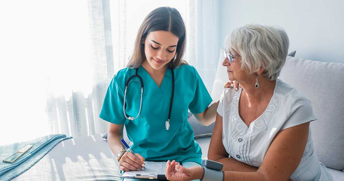 A nurse with her hand on a patients shoulder, taking notes, on national nurses week