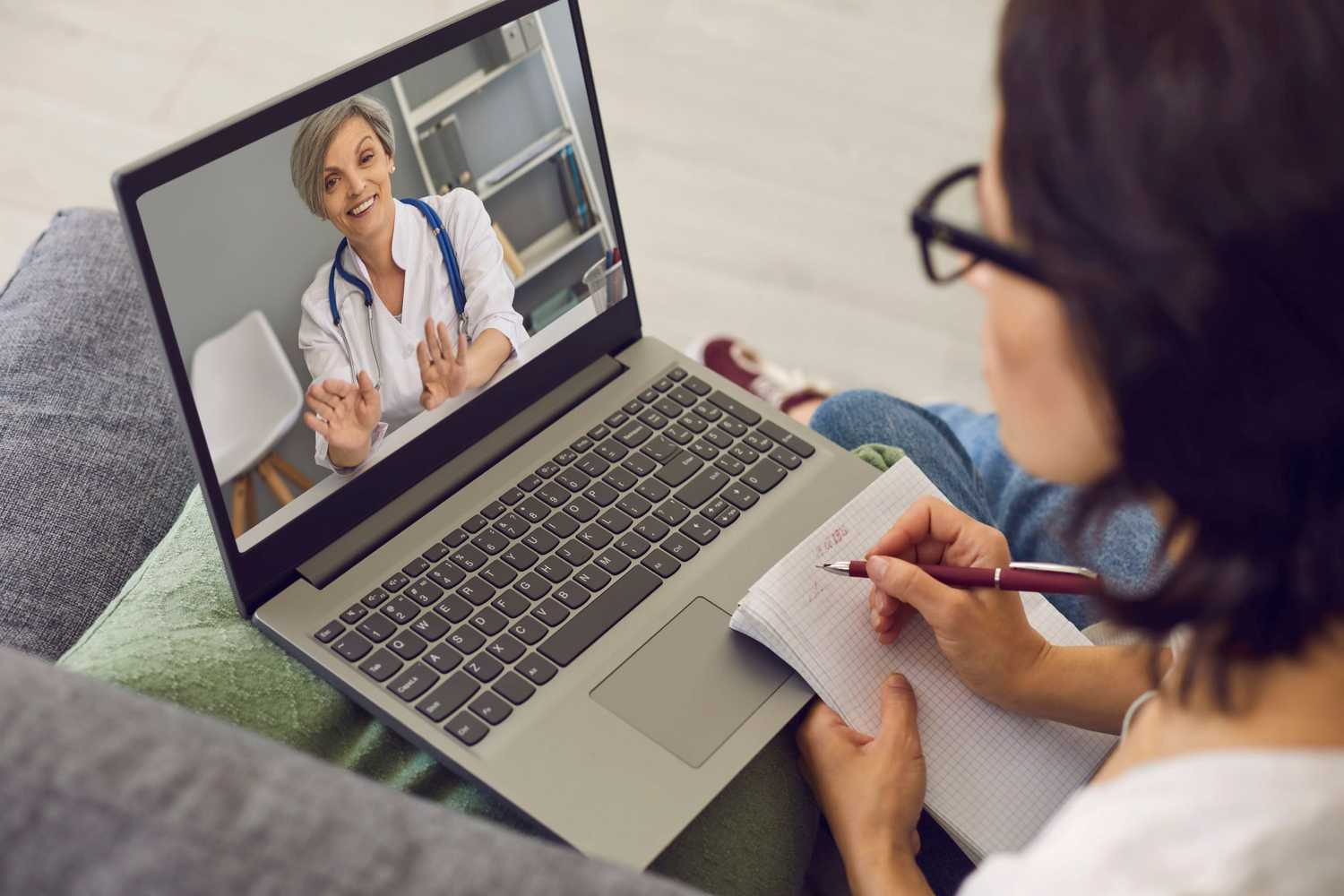 A female patient taking notes while on a telehealth visit with a doctor