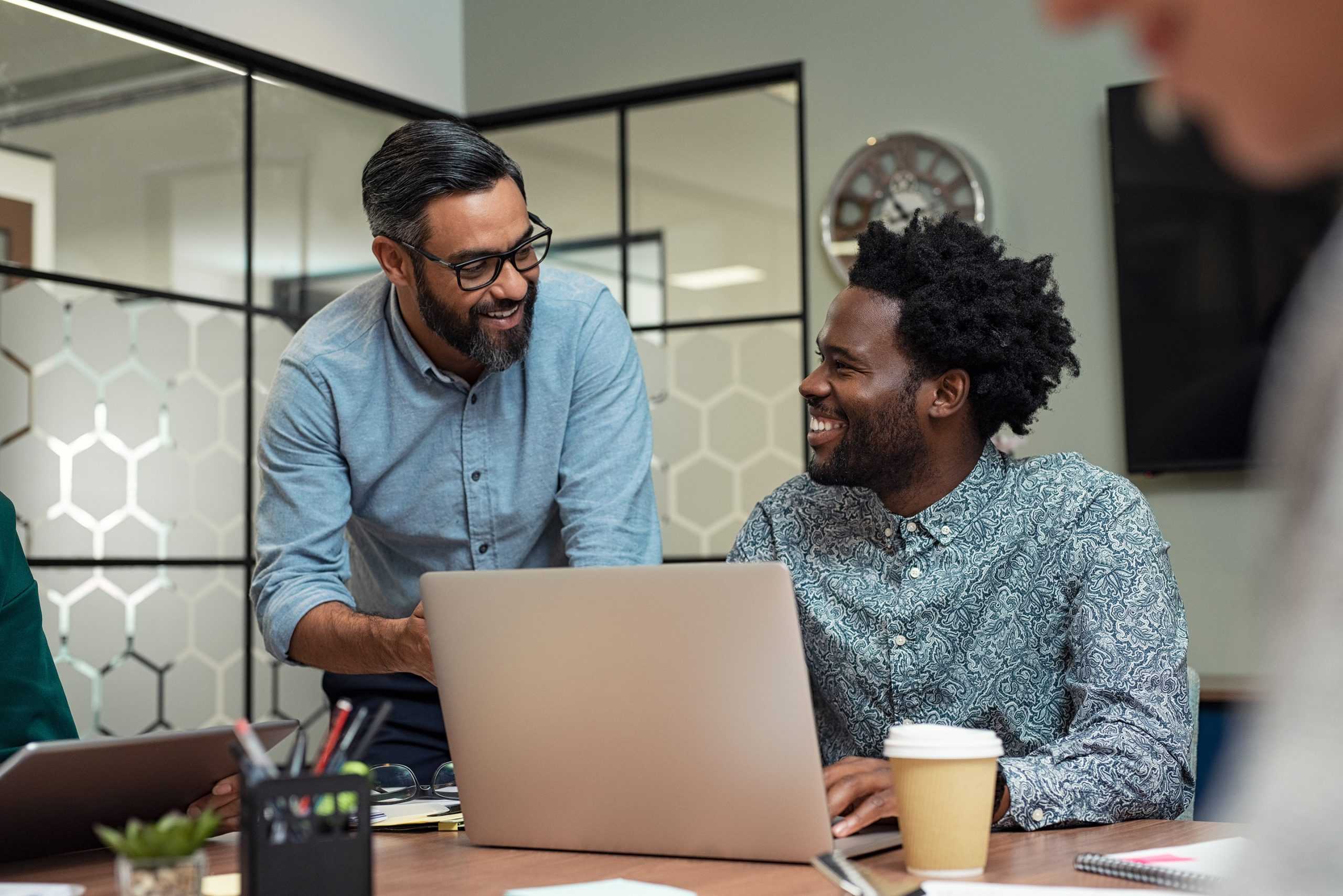 a return to work coordinator on his laptop smiling and listening to his colleague at work