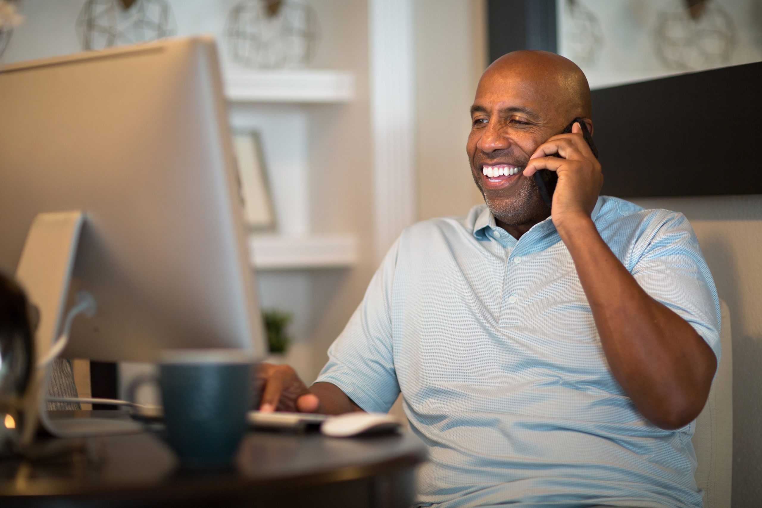 a happy man on his computer and on a phone call with a return to work coordinator