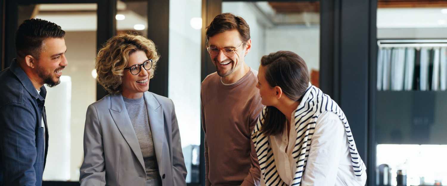 Happy group of coworkers standing around desk collaborating on claims management