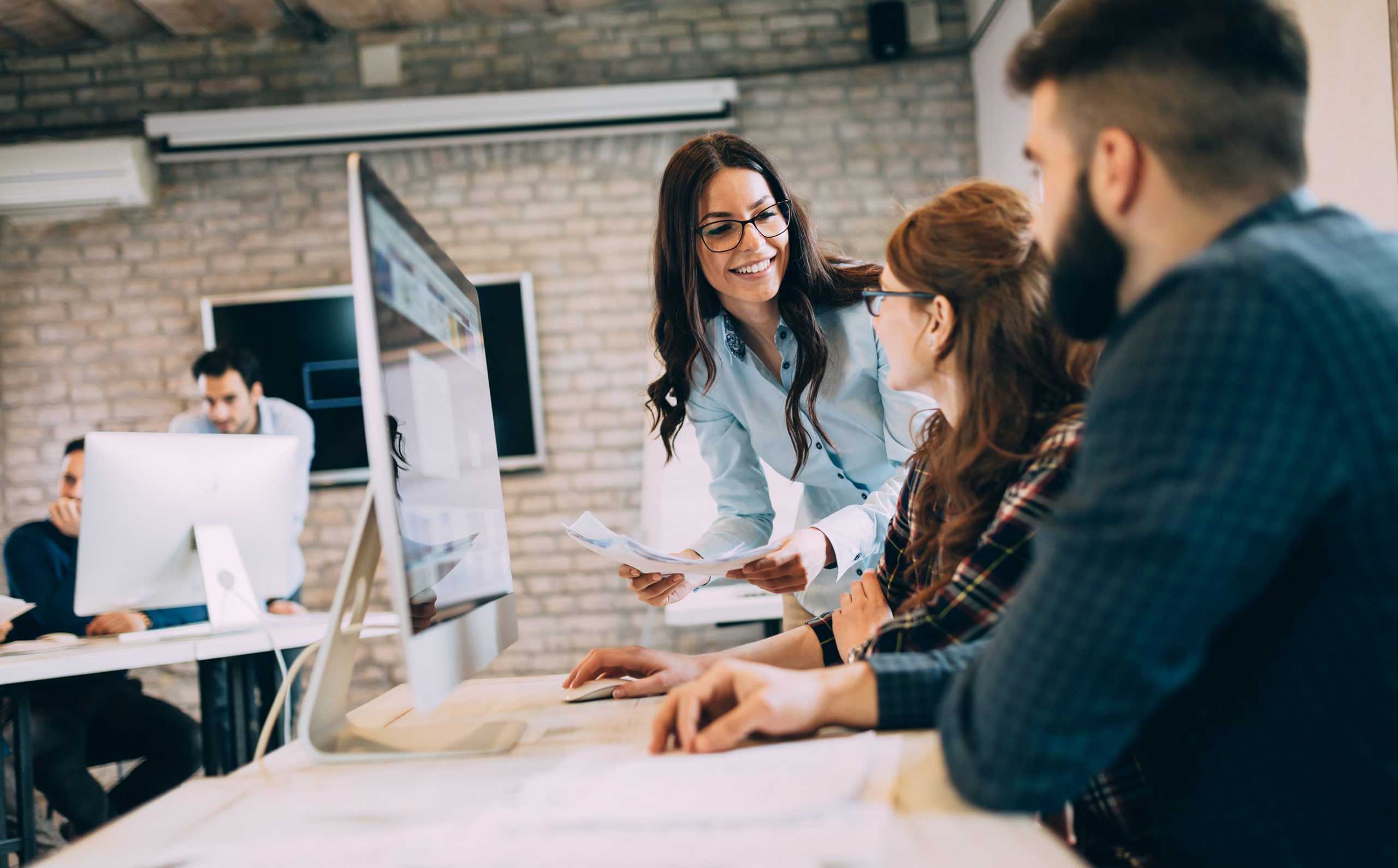 a female vocational case manager leaning over and instructing transitional work duties to two employees sitting at a desk