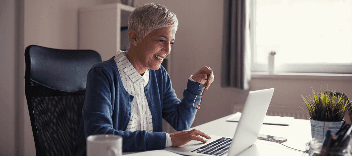 A woman smiling at her computer, working from a desk in her home