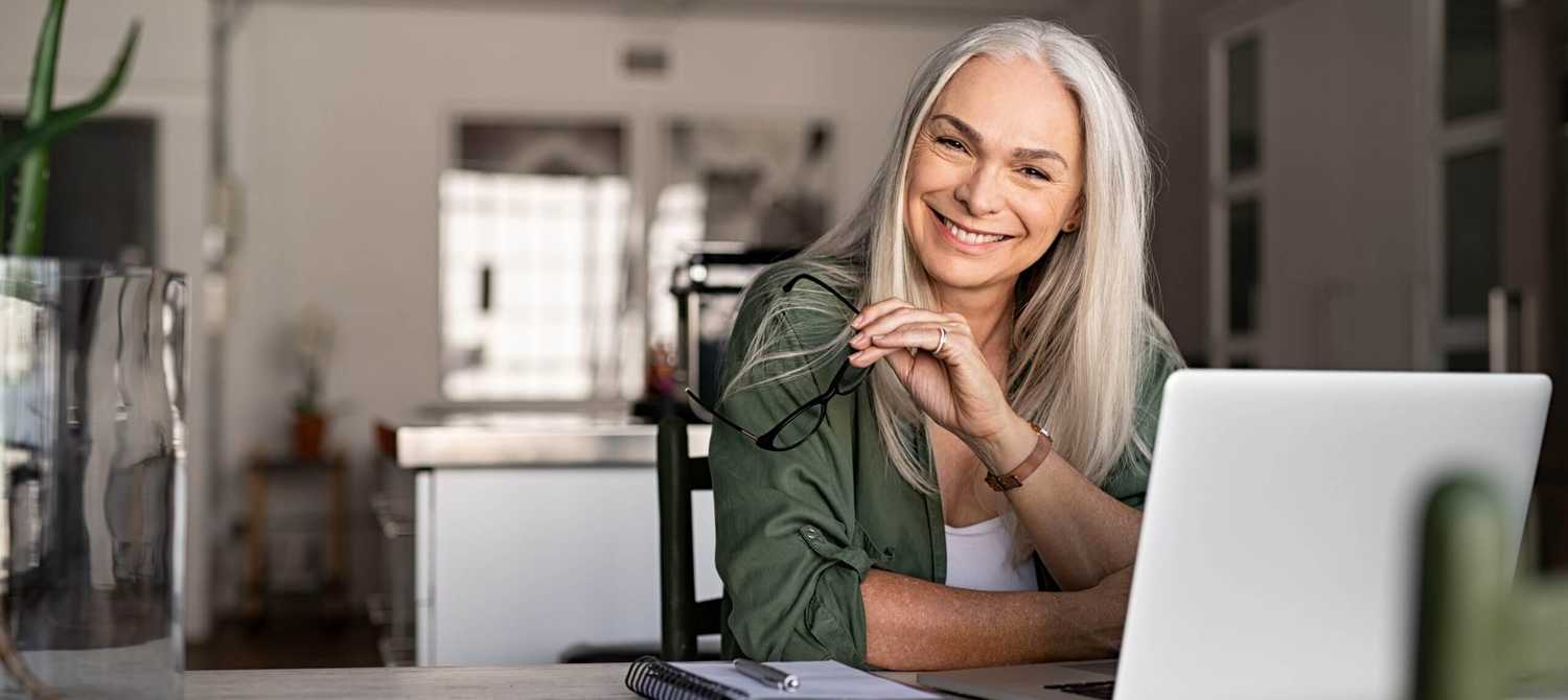 Portrait of happy senior woman holding eyeglasses and looking at camera at home. Successful old lady laughing and working at home. Beautiful stylish elderly woman smiling and relaxing at home.