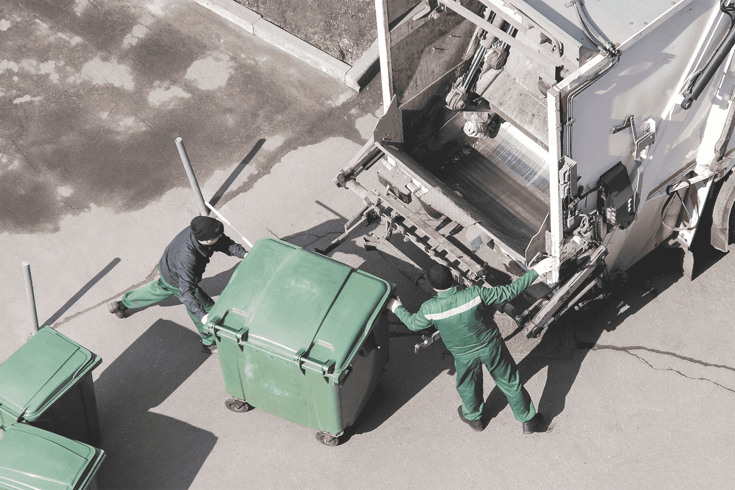 Two Recology employees loading garbage bins into their truck.