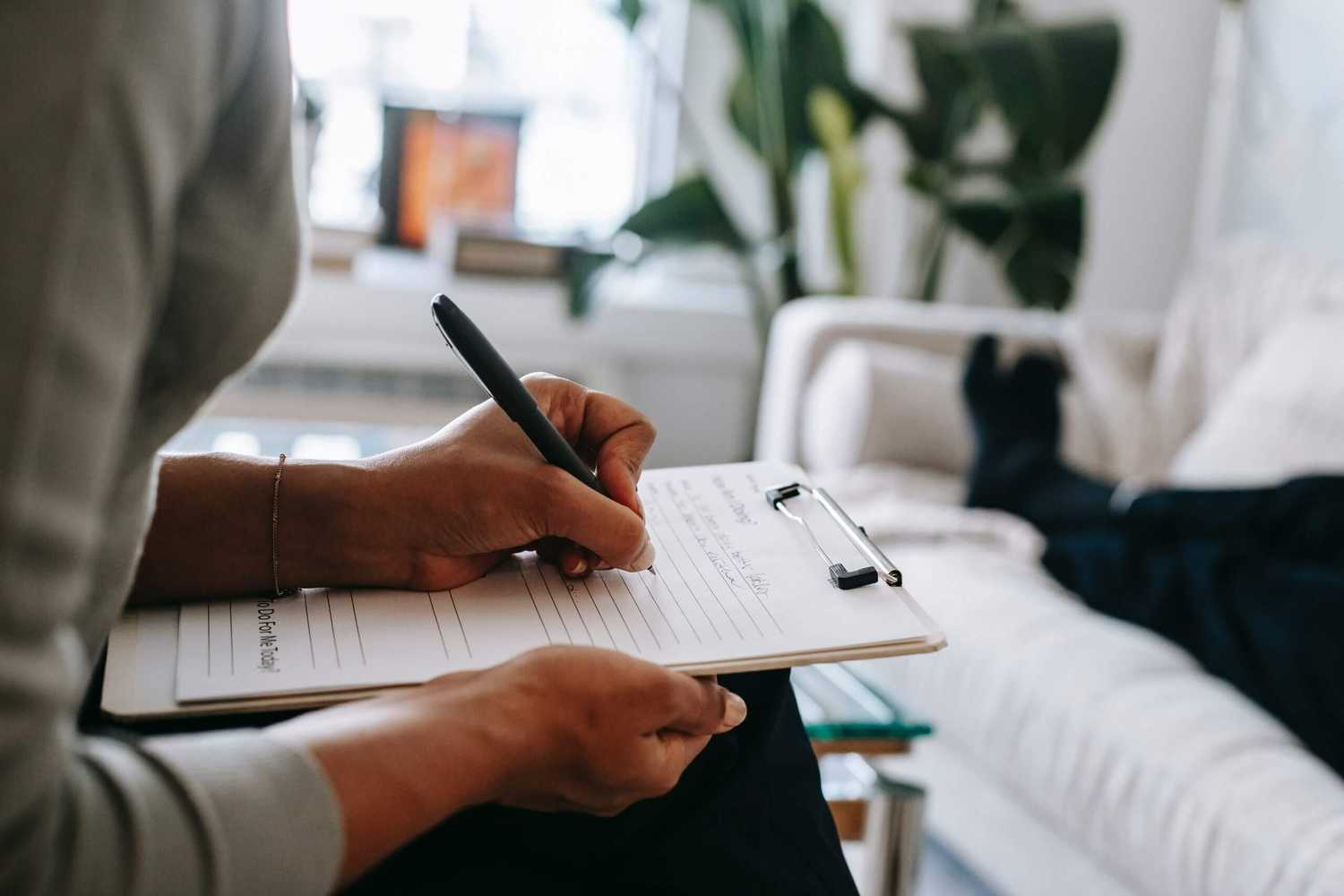 A person filling out a claim form, while another person is laying down on a couch in front of them.