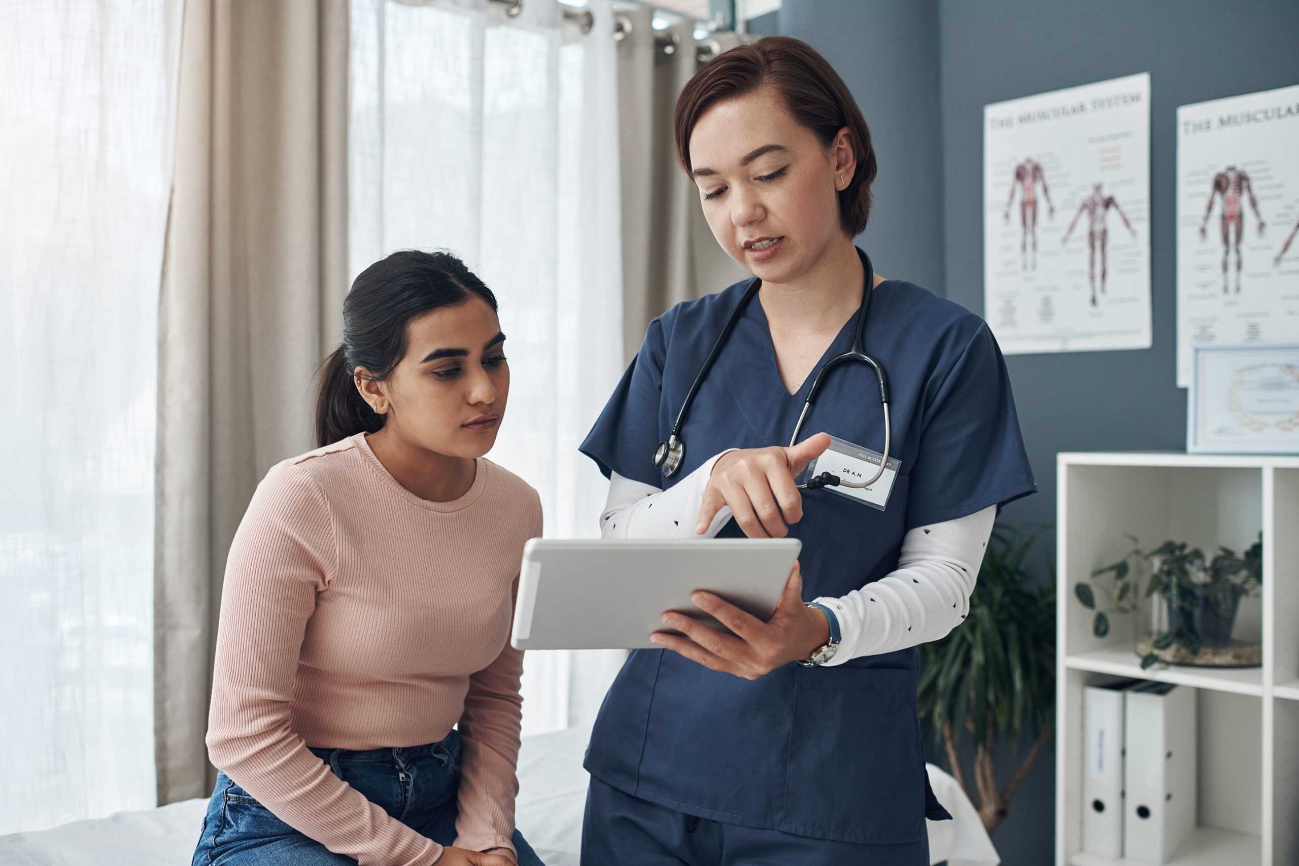 a female nurse with a young woman going over medical results on a tablet